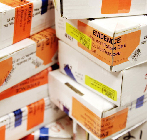 Stack of white evidence boxes with orange labels saying "Evidence. Warning!! Police Seal Do Not Remove" 